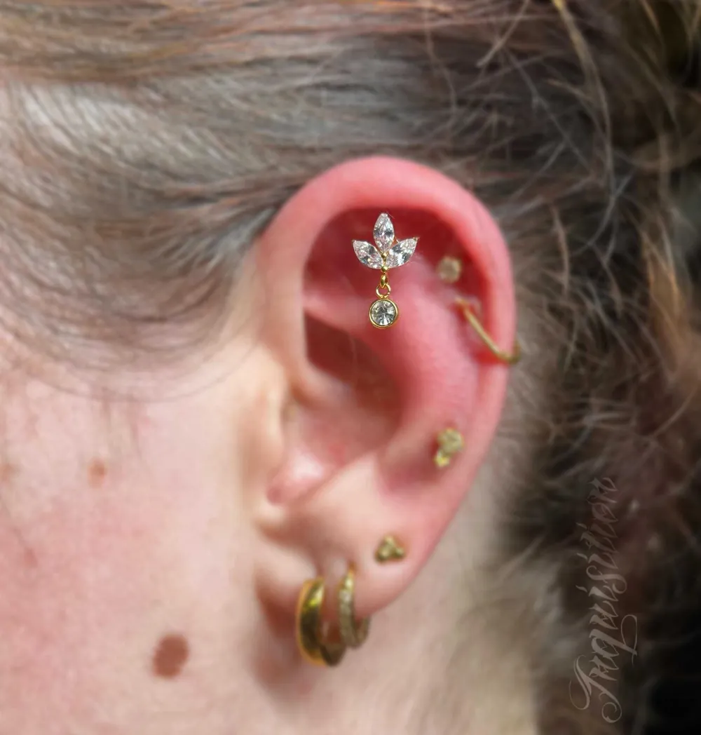 Gouden lotusjuweel met hangend steentje in een flat piercing, met een helix ring en kleine gouden studs in het oor