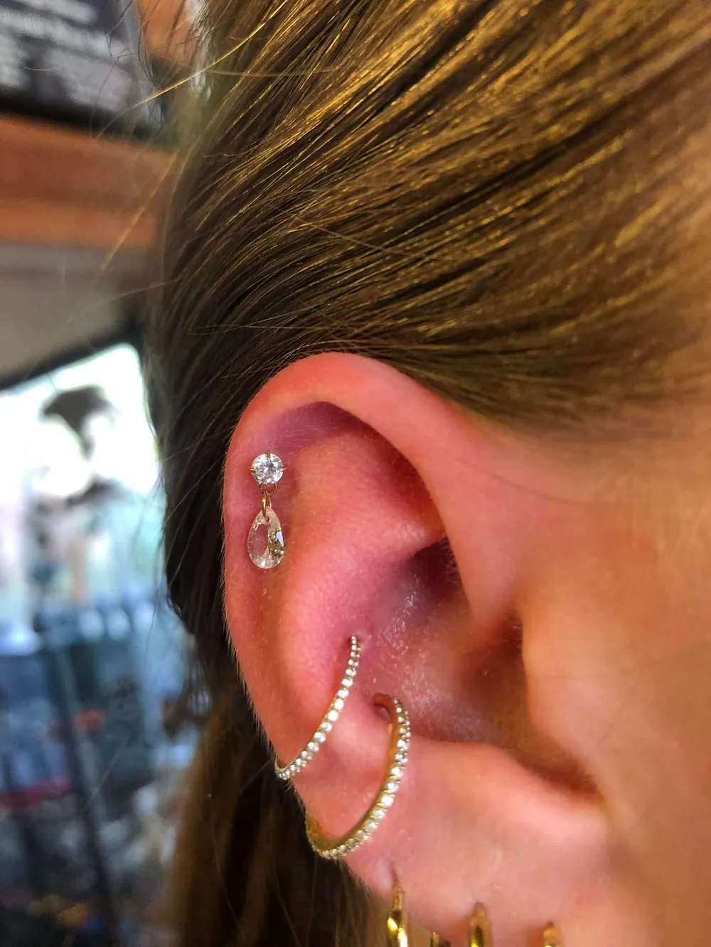 Helix piercing met hangende druppelsteen en twee gouden conch ringen bezet met steentjes