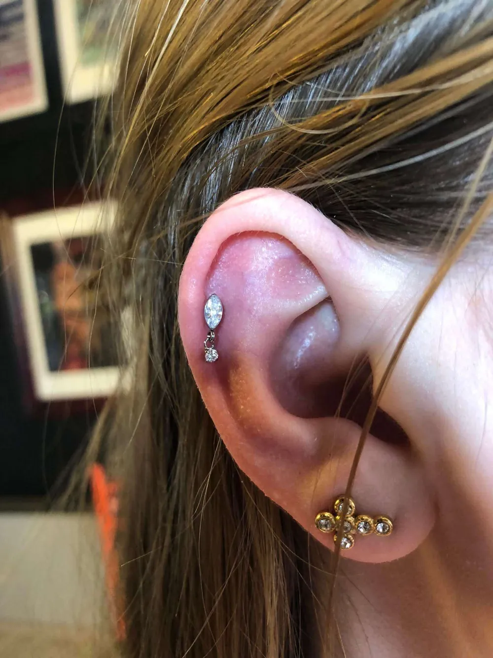 Helix piercing met een marquise-steen en hangend steentje, en een gouden kruisjuweel in de oorlel