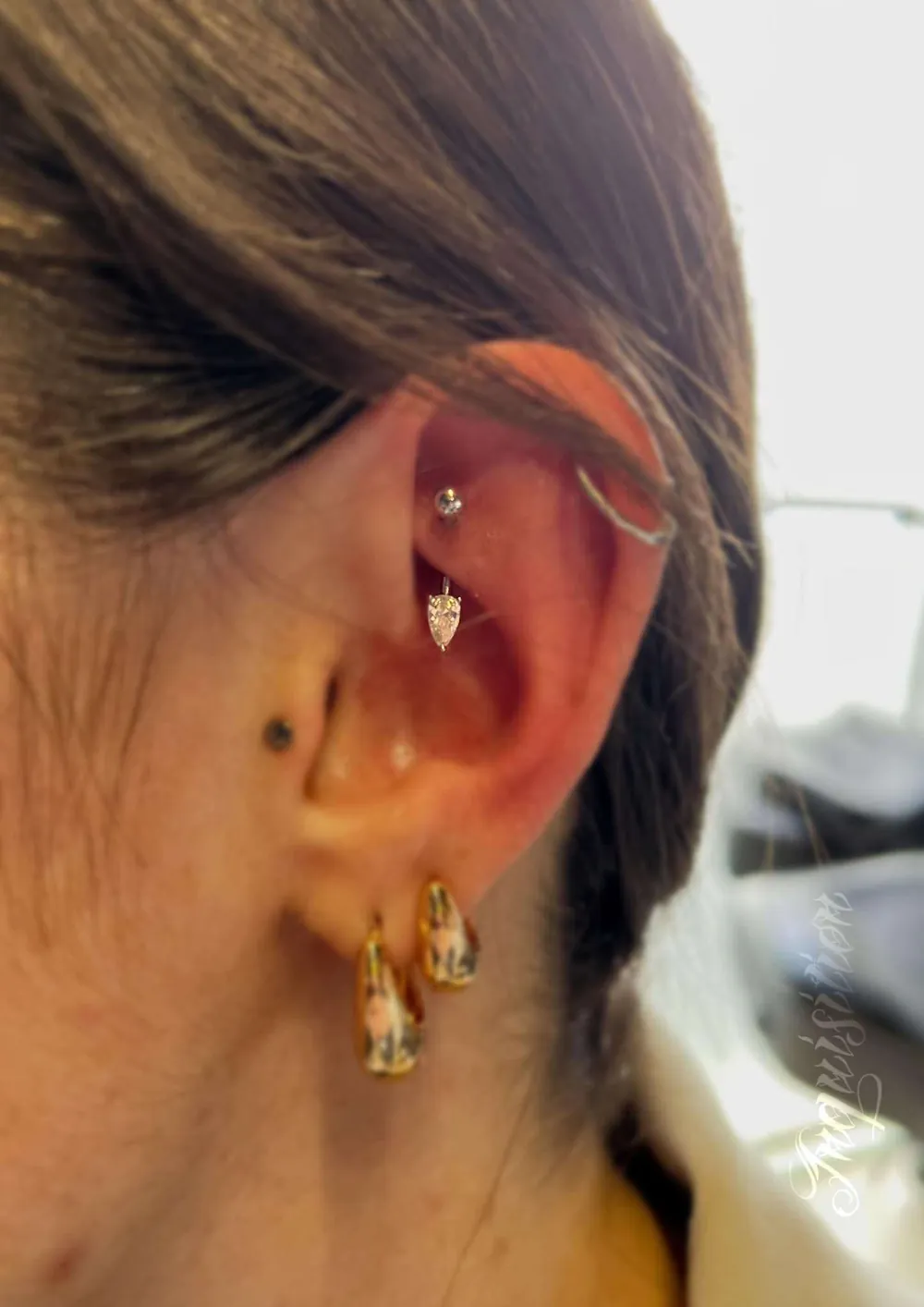 Rook piercing met druppelvormig steentje, een zilveren helix ring, een tragus stud en gouden oorbellen in de oorlel